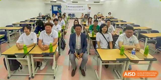 A classroom full of students is posing for a group photo, with a male teacher or guest sitting in the front row, at Guokai International School of Qingdao.