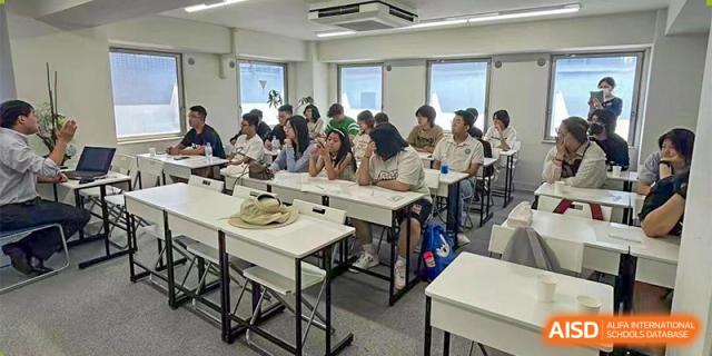 A group of students is seated at desks, engaged in a discussion or lesson in a brightly lit classroom at Guokai International School of Qingdao.