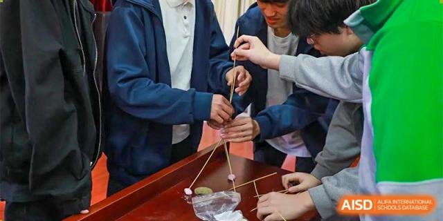 A close-up of students working together on a team-building or engineering project using sticks and string at Guokai International School of Qingdao.