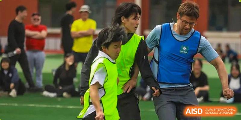 Two people, one wearing a bright yellow-green vest, walking together during an outdoor activity at Guokai International School of Qingdao.
