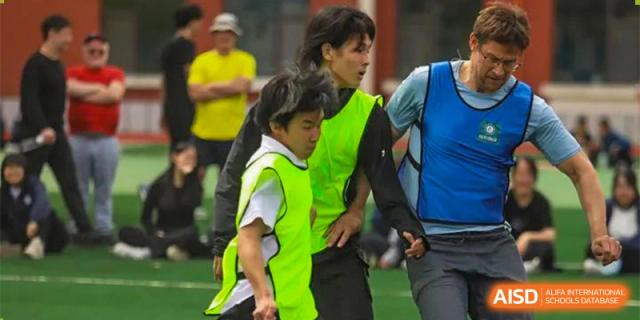 Two people, one wearing a bright yellow-green vest, walking together during an outdoor activity at Guokai International School of Qingdao.