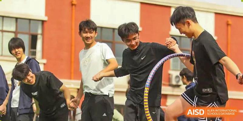 Two male students smile while playing with a hula hoop outdoors at Guokai International School of Qingdao.