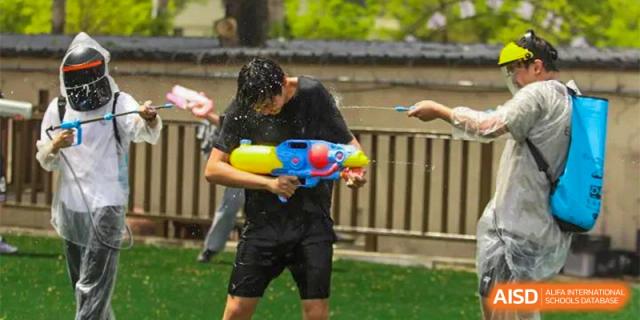 A male student, soaked with water, holds a large colorful water gun during a water fight activity at Guokai International School of Qingdao.