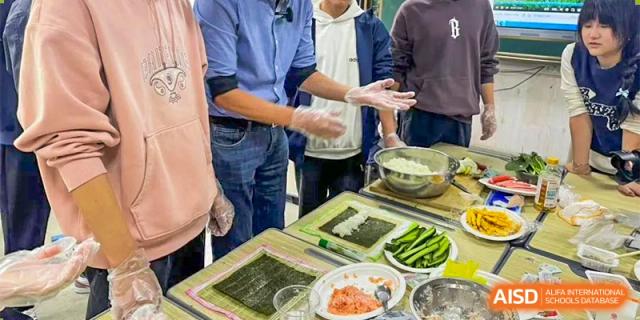 Students are participating in a sushi-making or cooking class, arranging rice and ingredients on nori seaweed at Guokai International School of Qingdao.