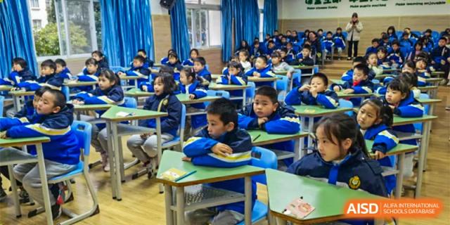 A boy in a striped shirt is looking down at his desk while other students are visible in the background at Chengdu Meishi International School.