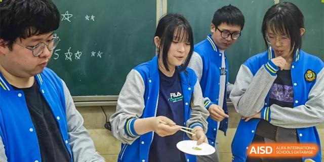 A student in a blue and white jacket is using chopsticks to pick up food from a plate at Chengdu Meishi International School.