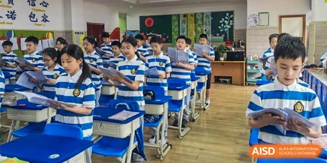 A line of male students in blue and white striped shirts are standing by their desks in a classroom at Chengdu Meishi International School.