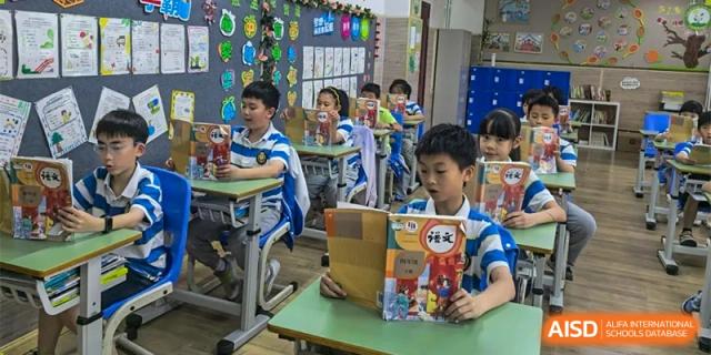 A student is sitting at his desk, reading a book, while another student is looking at the camera at Chengdu Meishi International School.