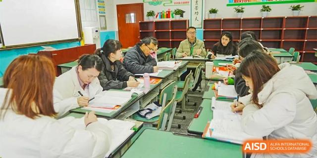 Students and a teacher are working together at a green desk in a classroom at Chengdu Meishi International School.
