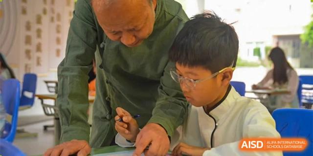 An adult is helping a student in glasses with a book at Chengdu Meishi International School.