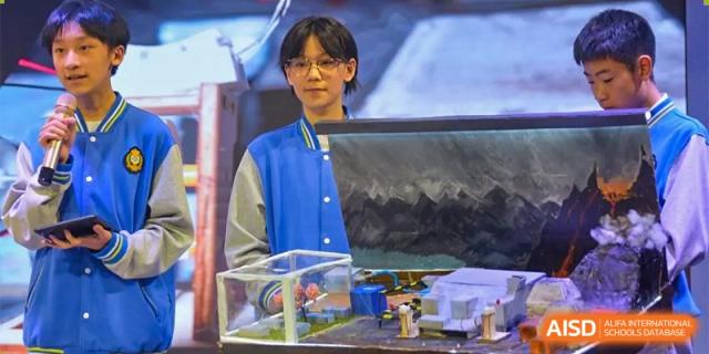 A young man in a blue and white jacket is looking at the camera while standing next to a science project at Chengdu Meishi International School.