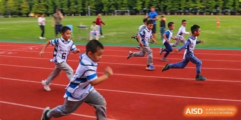 Students from Chengdu Meishi International School running on a red track during a sports day event, with others watching from the stands.