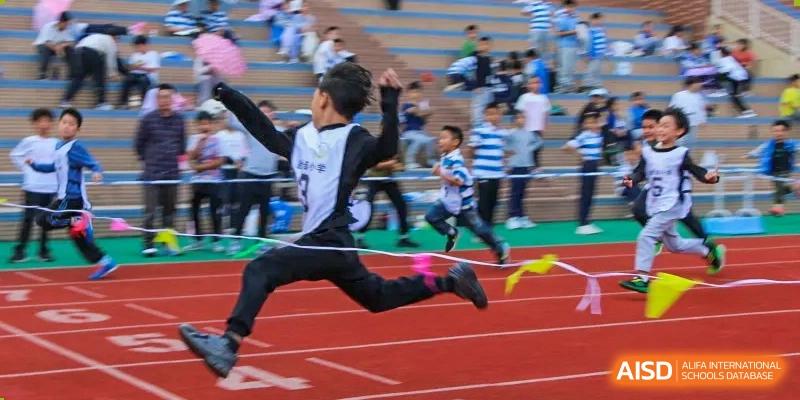 A student from Chengdu Meishi International School jumping with a ribbon in hand, celebrating a victory or a finish during a race.