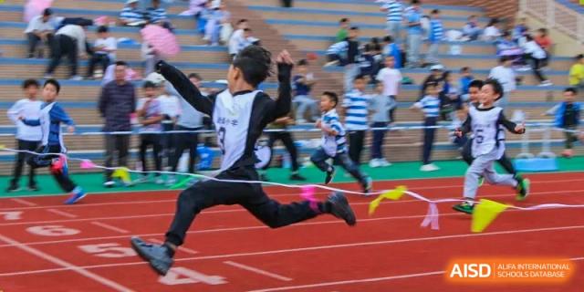 A student from Chengdu Meishi International School jumping with a ribbon in hand, celebrating a victory or a finish during a race.