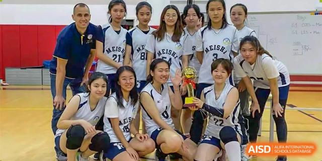 A group of female students, dressed in basketball uniforms, posing with a large trophy after a game at Chengdu Meishi International School.