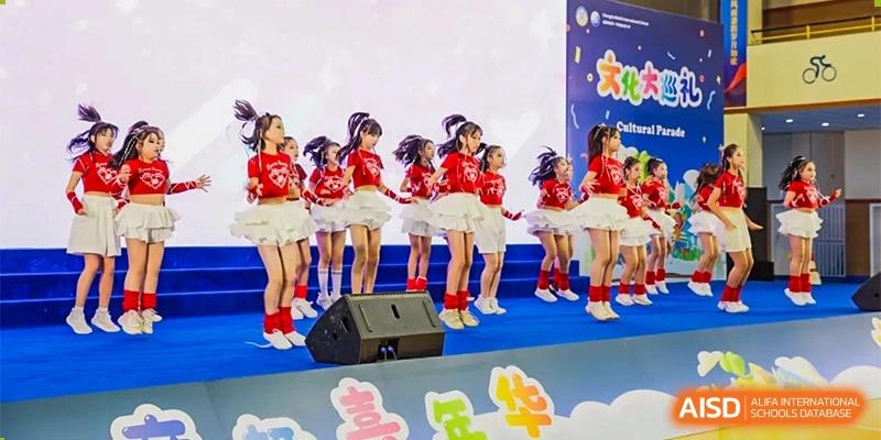 A group of young female students in matching red tops and white skirts performing a dance on a stage at Chengdu Meishi International School.
