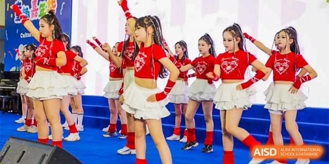 A close-up of a female student in a red crop top and white ruffled skirt posing with her hands on her hips during a performance at Chengdu Meishi International School.