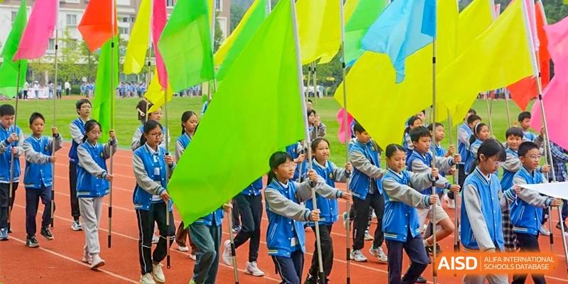 Students holding large, brightly colored flags in green, yellow, and blue, standing together at an outdoor event at Chengdu Meishi International School.