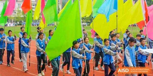 Students holding large, brightly colored flags in green, yellow, and blue, standing together at an outdoor event at Chengdu Meishi International School.