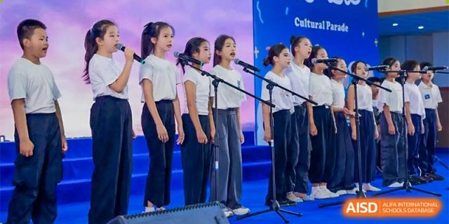 A group of female students are singing on a stage with microphones in front of a blue backdrop at Chengdu Meishi International School.
