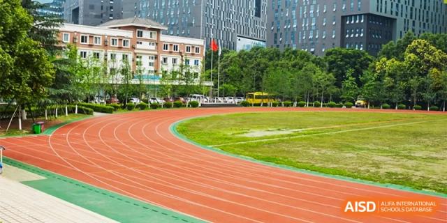 A wide shot of the school's running track and green field with the main school building in the background at Chengdu Meishi International School.