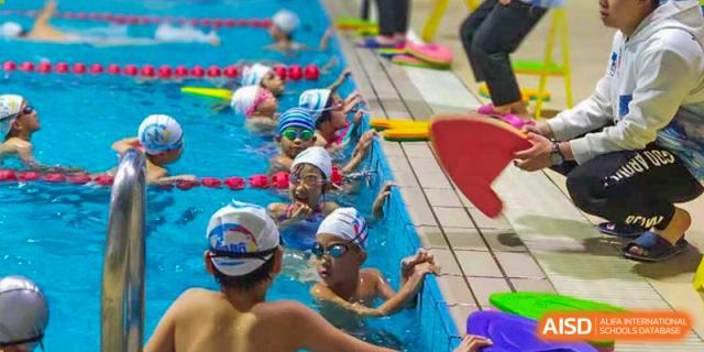 Students in swim caps and goggles are lined up at the edge of a swimming pool at Chengdu Meishi International School.