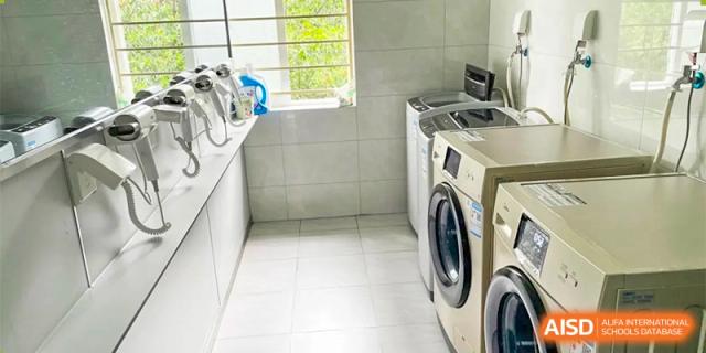 An image of a laundry room with a washing machine and a white tile floor at Chengdu Meishi International School.