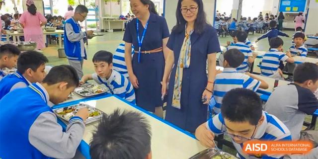 Students in blue and white striped shirts are eating a meal in the cafeteria at Chengdu Meishi International School.