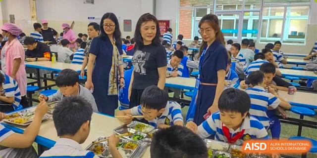 A woman is standing over a table as students eat their meals at Chengdu Meishi International School.