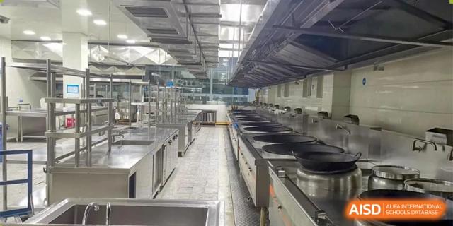 A long, clean, stainless steel kitchen with cooking equipment and vents at Chengdu Meishi International School.