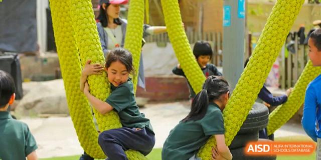 A young Qingdao Cornerstone Bilingual School student smiling while climbing on outdoor playground equipment.