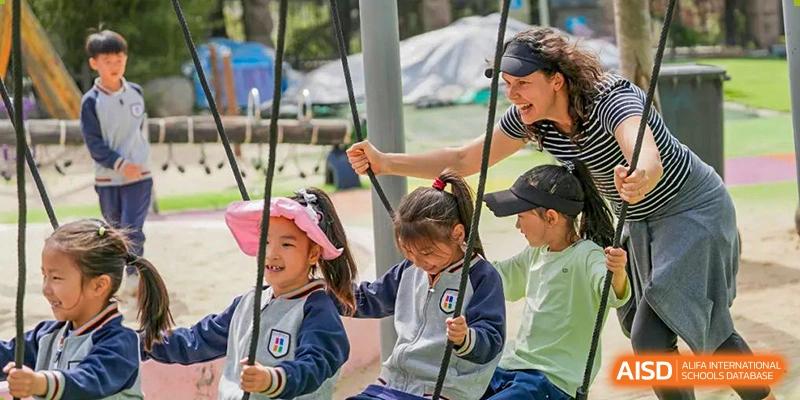 A Qingdao Cornerstone Bilingual School teacher helping a student on a swing on the playground.