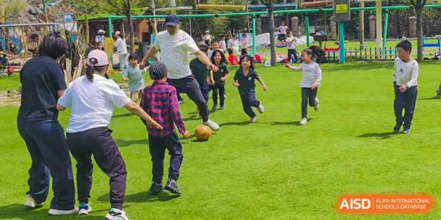 A group of Qingdao Cornerstone Bilingual School students running with a ball on the sports field.