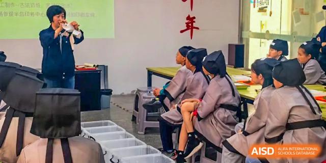 Qingdao Cornerstone Bilingual School students in traditional Chinese robes seated during a school performance or event.