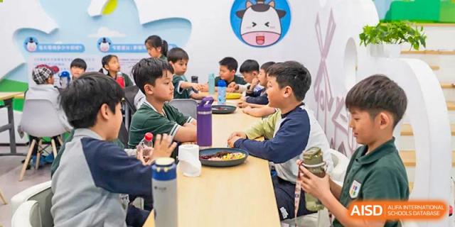 A group of Qingdao Cornerstone Bilingual School students sitting at a long table and eating a meal together.