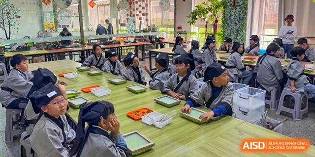 A large group of Qingdao Cornerstone Bilingual School students in traditional Chinese clothing working on a project at a table.