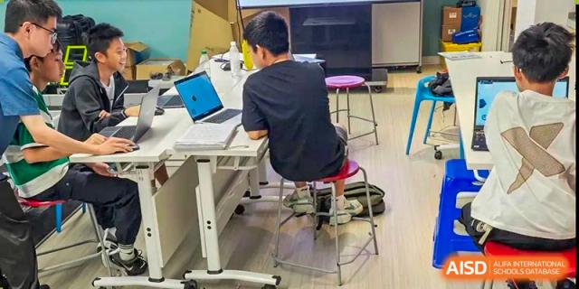 A student from Tsinglan School sitting at a desk and using a laptop in a classroom.