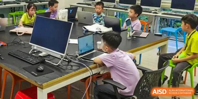 Students from Tsinglan School sitting at a long table and using laptops in a classroom.