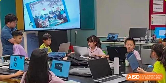 Students from Tsinglan School sitting at a long table and working on laptops in a classroom, with a presentation on the screen in the background.