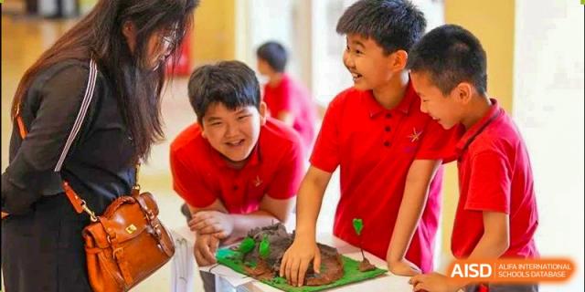 Two male students from Tsinglan School in red shirts, smiling and working together on a project in a classroom.