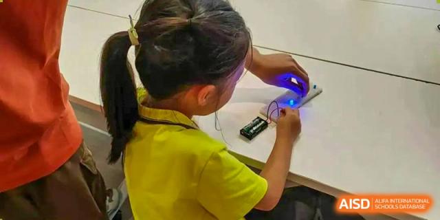 A young student from Tsinglan School using a tool to work on a small, electronic project in a classroom.