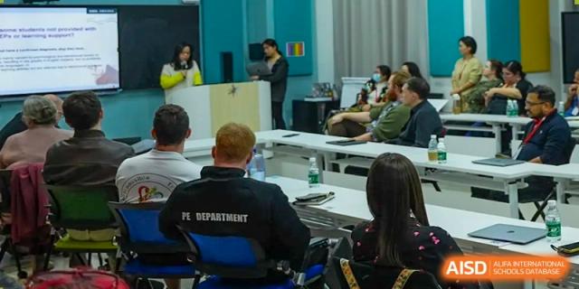 Students and a teacher from Tsinglan School sitting in a classroom, with a person in a police department t-shirt in the background.