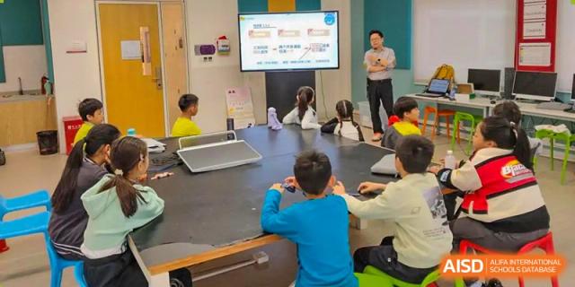 A teacher from Tsinglan School giving a presentation to a group of students sitting at a table in a classroom.