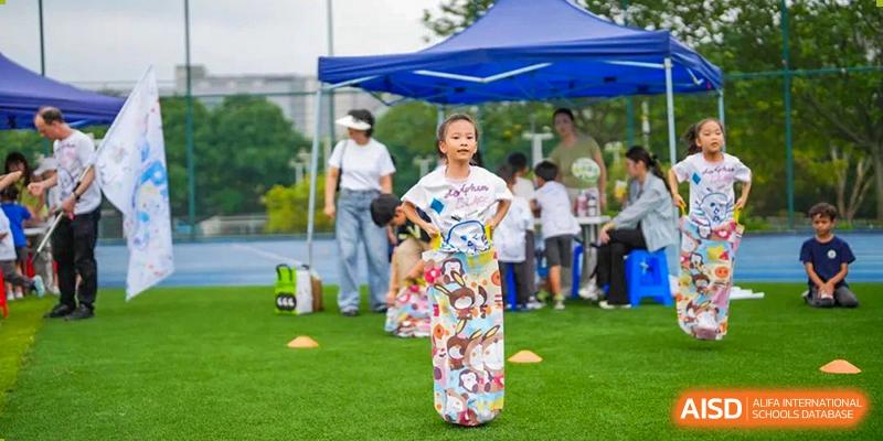 A young student from Tsinglan School participates in a sack race at an outdoor sports event.