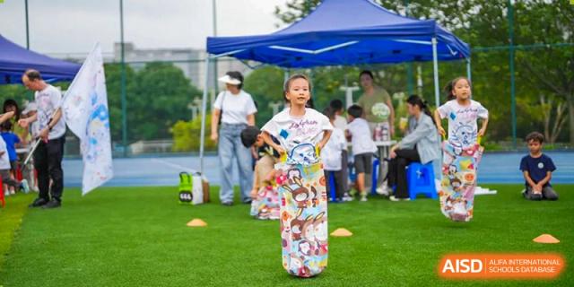A young student from Tsinglan School participates in a sack race at an outdoor sports event.