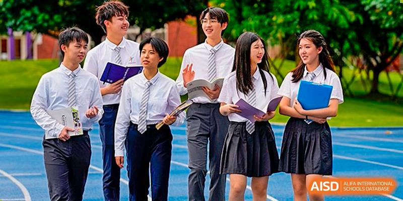 A group of students from Tsinglan School, dressed in uniforms, walk and talk outside on a sunny day.