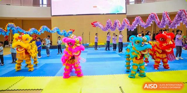 Young children from Tsinglan School performing a traditional lion dance on a blue mat.