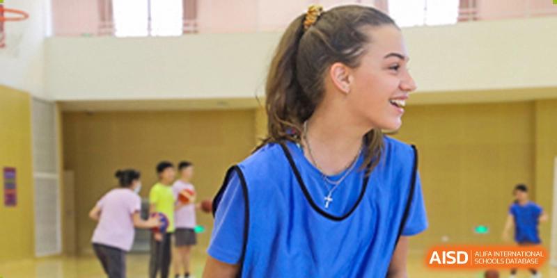A student from Tsinglan School, wearing a blue jersey and a cross necklace, watching a game with her hair tied up.