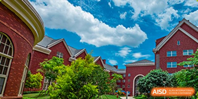 A beautiful shot of the red brick building and trees on the campus of Tsinglan School under a blue sky with white clouds.