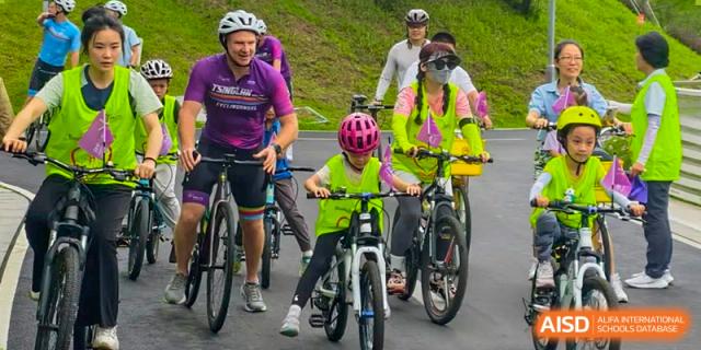 Students and teachers from Tsinglan School riding bicycles in a group outdoors, with some wearing yellow vests and helmets.